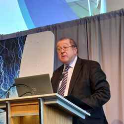 Graeme Dey MSP faces out towards the crowd (out of shot) while standing in front of a lecturn and a laptop